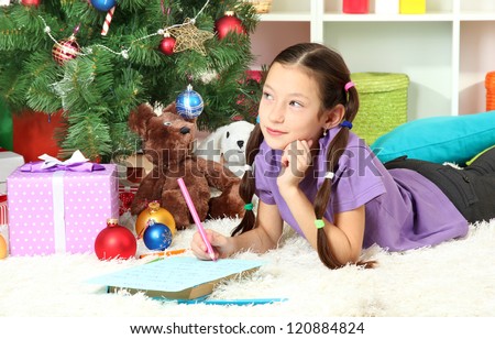 Little girl writing letter to Santa near christmas tree
