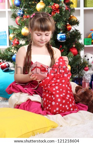 A little girl gets gifts from bag of Santa Claus in festively decorated room
