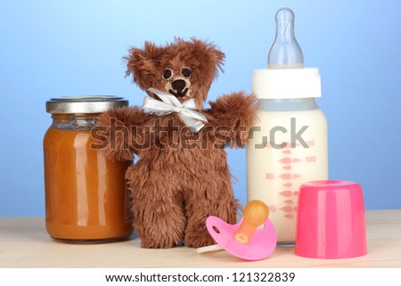 Baby food, bottle of milk, puree with teddy bear on blue background