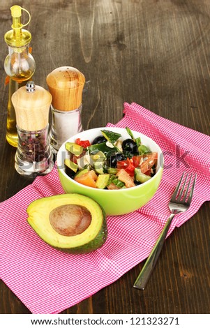 Tasty avocado salad in bowl   surrounded by spices on wooden table close-up