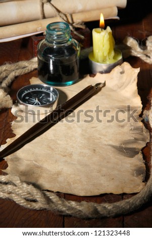 Old paper with ink pen near lighting candle on wooden table