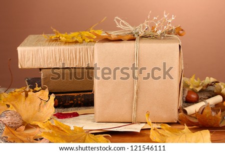 Autumnal composition with gift, books and leaves on brown background