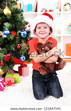 Little boy in Santa hat sits near Christmas tree with gift in hands