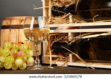Wooden case with wine bottle, barrel, wineglass and grape on wooden table on grey background