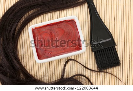 hair dye in bowl and brush for hair coloring on beige bamboo mat, close-up