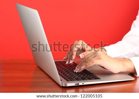 business woman\'s hands typing on laptop computer, on red background close-up
