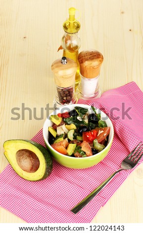 Tasty avocado salad in bowl   surrounded by spices on wooden table close-up