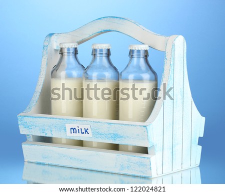 Milk in bottles in wooden box on blue background
