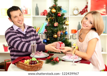 Young happy couple with presents sitting   at table near Christmas tree