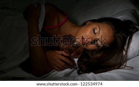 young beautiful woman with fluffy bear sleeping in bed in dark bedroom