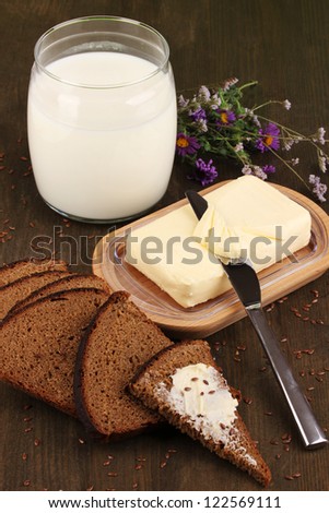 Butter on wooden holder surrounded by bread and milk on wooden table close-up