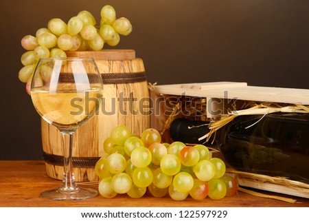 Wooden case with wine bottle, barrel, wineglass and grape on wooden table on brown background
