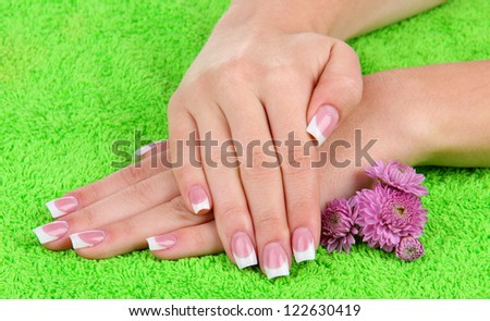 Woman hands with french manicure and flowers on green towel