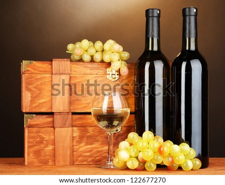 Wooden cases with wine bottles on wooden table on brown background