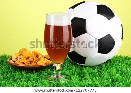 Glass of beer with soccer ball on grass on green background