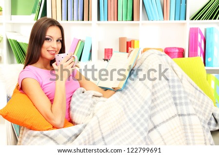Portrait of female with cup of tea reading book while lying on couch