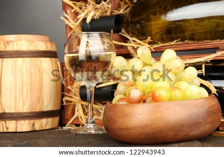 Wooden case with wine bottles, barrel, wineglass and grape on wooden table on grey background