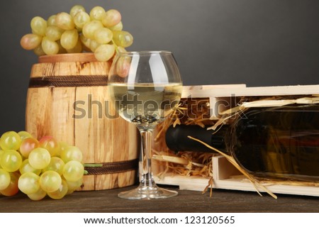 Wooden case with wine bottle, barrel, wineglass and grape on wooden table on grey background