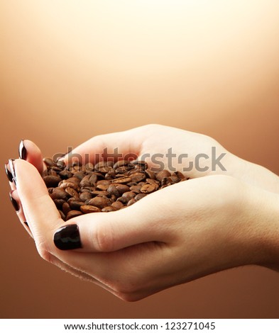 female hands with coffee beans, on brown background