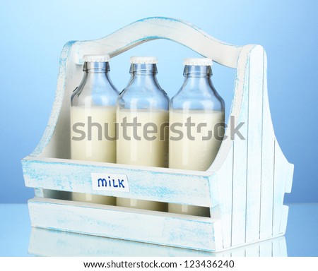 Milk in bottles in wooden box on blue background