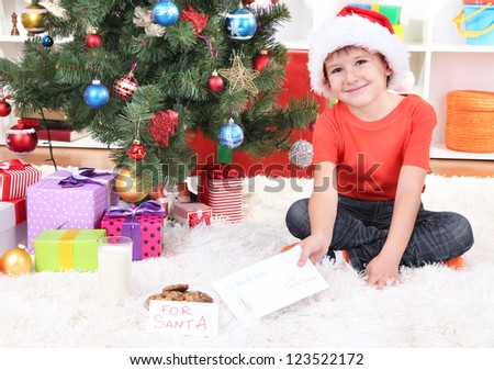 Little boy in Santa hat with milk, cookies and letter for Santa Claus