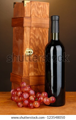 Wooden case with wine bottle on wooden table on brown background
