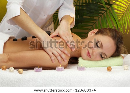 beautiful young woman in spa salon getting massage with spa stones, on green background