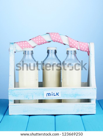 Milk in bottles in wooden box on blue wooden table on blue background