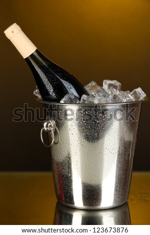 Bottle of wine in ice bucket on darck yellow background
