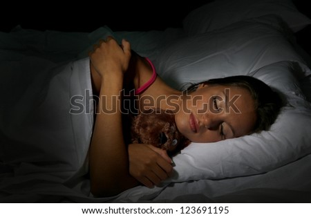 young beautiful woman with fluffy bear sleeping in bed in dark bedroom