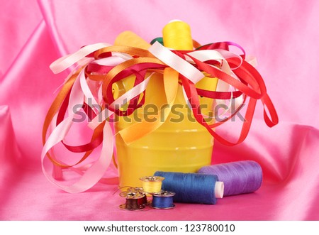 Color bucket with multicolor ribbons and thread on pink fabric background