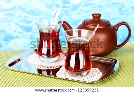 glass of Turkish tea and kettle on color background