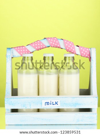Milk in bottles in wooden box on green background