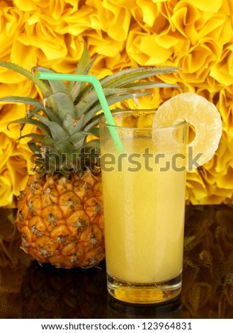 Ripe pineapple and juice glass on black table on yellow decorative background