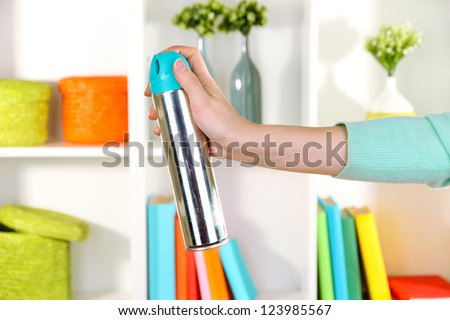 Sprayed air freshener in hand on white shelves background