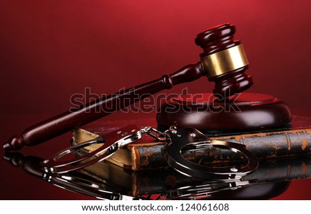 Gavel, handcuffs and book on law on red background