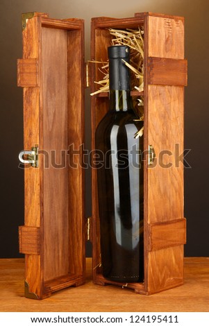 Wooden case with wine bottle on wooden table on brown background
