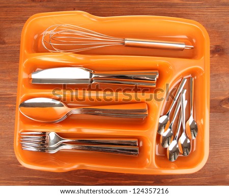 Orange plastic cutlery tray with checked cutlery on wooden table