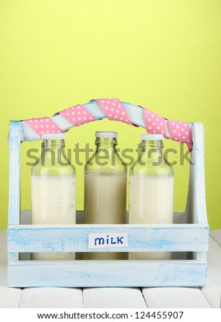 Milk in bottles in wooden box on wooden table on green background