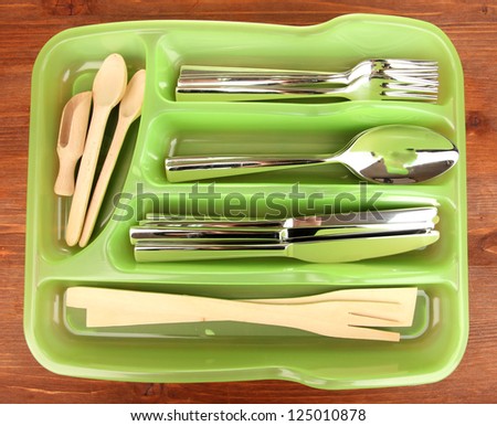 Green plastic cutlery tray with checked cutlery and wooden spoons on wooden table