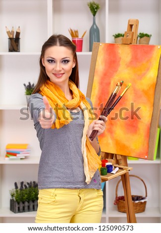 beautiful young woman painter at work, on room interior background