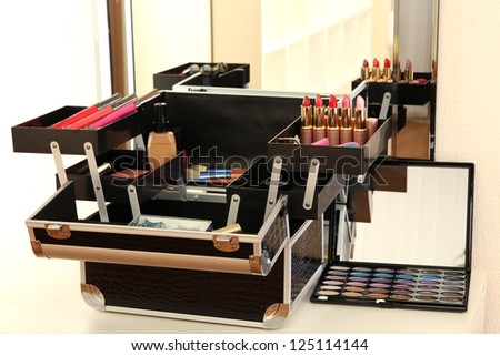 Open case with cosmetics on table near mirror