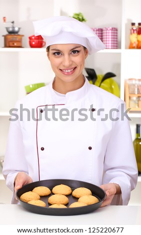 Young woman chef with cakes on dripping pan in kitchen