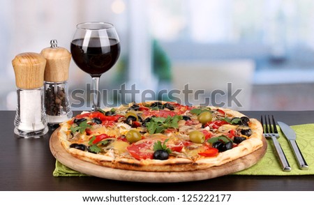 Delicious pizza with glass of red wine and spices on wooden table on room background