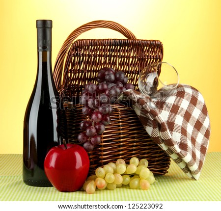 Picnic basket and bottle of wine on cloth on yellow background