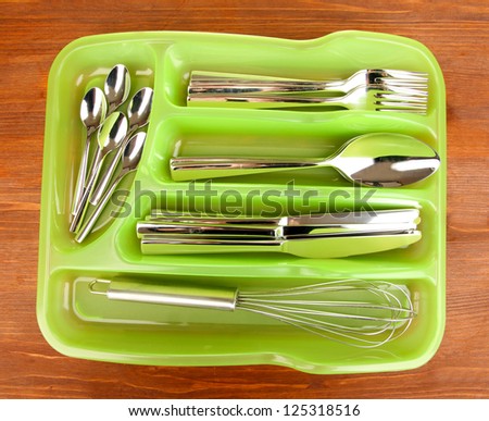 Green plastic cutlery tray with checked cutlery on wooden table