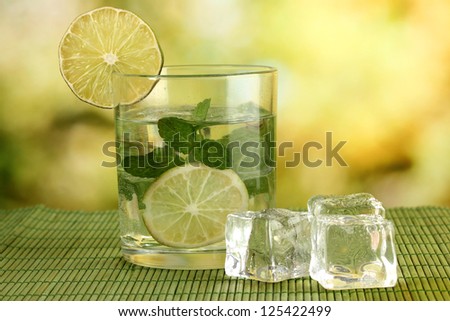 Glass of water with ice, mint and lime on table on bright background