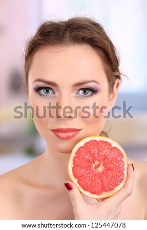 Beautiful young woman with bright make-up, holding grapefruit, on bright background