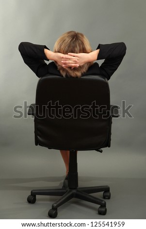 Young beautiful business woman resting on chair on grey background