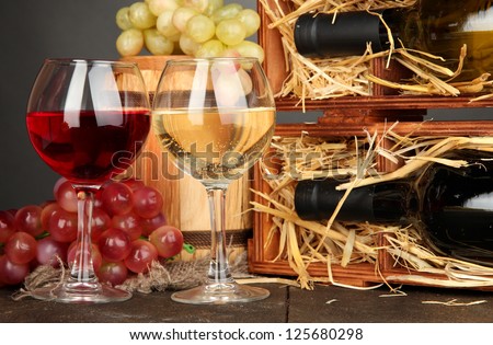 Wooden case with wine bottles, barrel, wineglasses and grape on wooden table on grey background